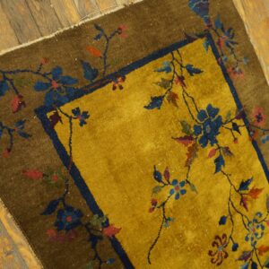 Gold and brown floral rug with a navy border rests on distressed wooden floorboards.