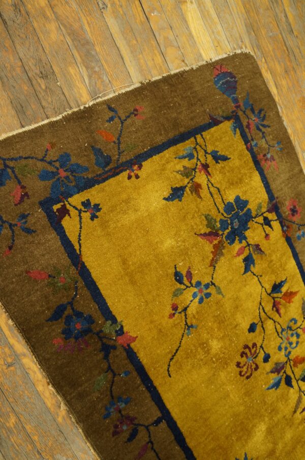 Gold and brown floral rug with a navy border rests on distressed wooden floorboards.