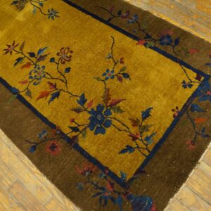 Gold rug with winding blue and red floral patterns framed by a dark brown border on distressed wood flooring.