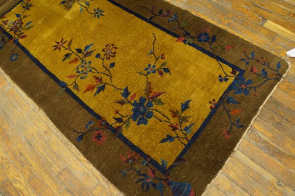 Gold rug with winding blue and red floral patterns framed by a dark brown border on distressed wood flooring.