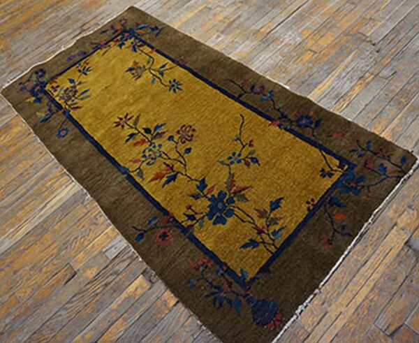 Mustard gold rug with olive border and navy floral patterns rests on distressed wooden planks.