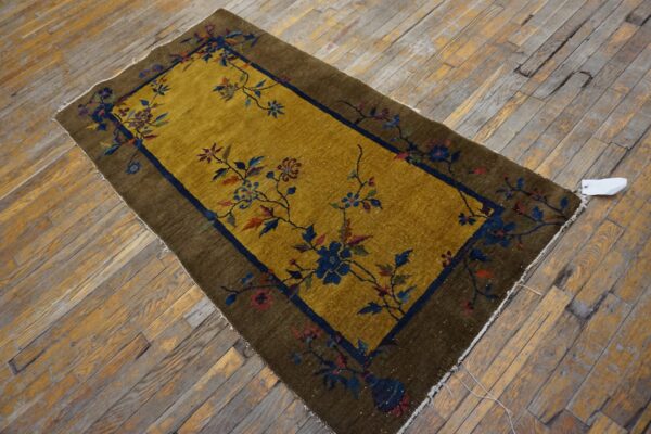 Gold field rug with a brown border and dark blue floral vines laid upon distressed wood flooring.