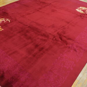 A large crimson rug with a wide tone-on-tone floral border and bright gold corner accents rests on wood floors.