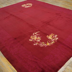 A large deep red rug with colorful floral medallions rests upon distressed yellow wood plank flooring.