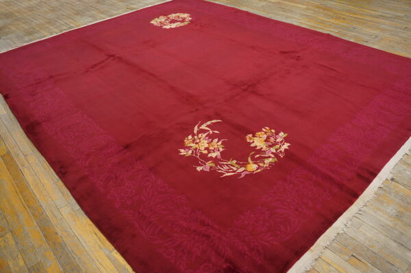 A large deep red rug with colorful floral medallions rests upon distressed yellow wood plank flooring.