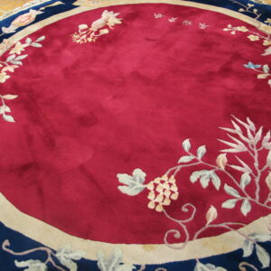 Round rug with a deep crimson center field, detailed floral pattern, and navy blue outer border on wood.