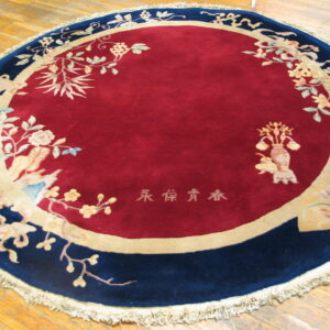 Round rug with a deep red center, navy border, and detailed botanical patterns on wood floors.