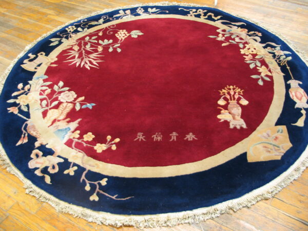 Round rug with a deep red center, navy border, and detailed botanical patterns on wood floors.
