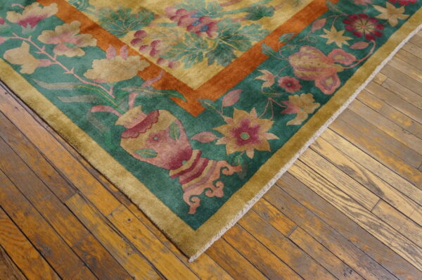 Gold and teal low-pile rug with complex floral motifs and a rust border on worn plank wood flooring.