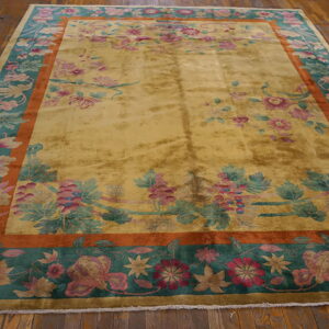 Lustrous gold rug with pink and teal botanical borders framed by rust stripes on wood planks.