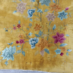 Plush yellow rug with colorful blue, pink, and orange floral sprays and visible fringe on gray pavement.