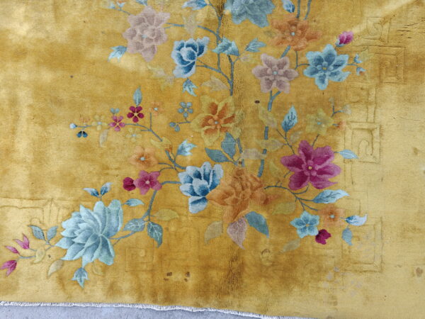 Plush yellow rug with colorful blue, pink, and orange floral sprays and visible fringe on gray pavement.