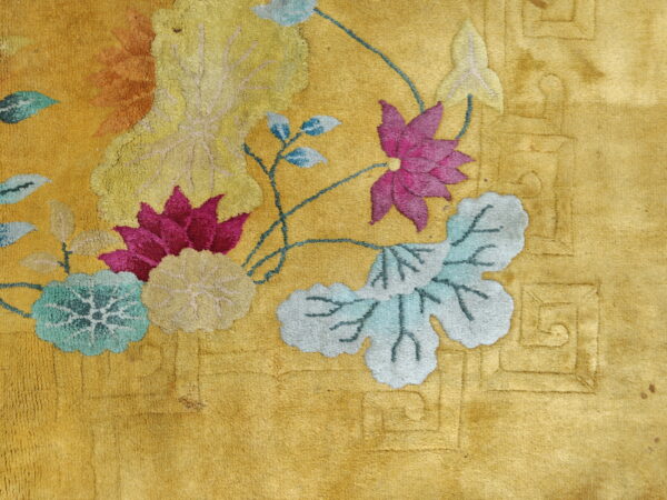 Golden yellow rug with detailed pink, blue, and teal floral motifs and embossed geometric patterns in the border area.