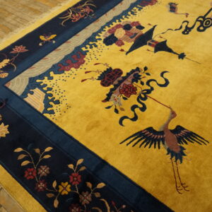 Mustard yellow rug with navy borders displays detailed cranes and floral patterns on wood plank flooring.