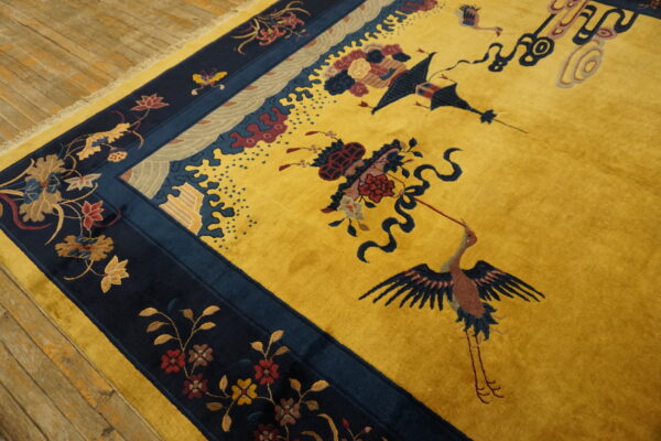 Mustard yellow rug with navy borders displays detailed cranes and floral patterns on wood plank flooring.