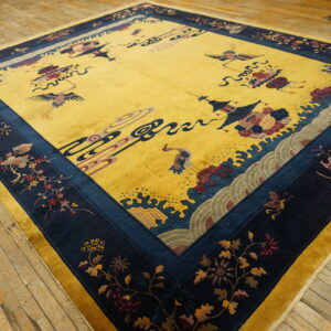 Gold rug with a navy blue border displays stylized cranes and floral motifs on aged wood flooring.