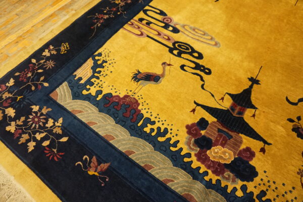 Detailed gold rug with navy border shows a crane, pagoda, and complex floral and wave patterns.