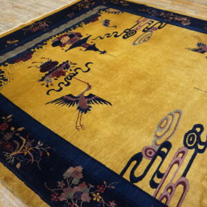 Mustard yellow high-pile rug with a navy blue border featuring detailed crane and floral patterns on wood flooring.