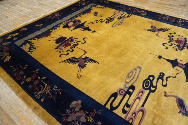 Mustard yellow high-pile rug with a navy blue border featuring detailed crane and floral patterns on wood flooring.
