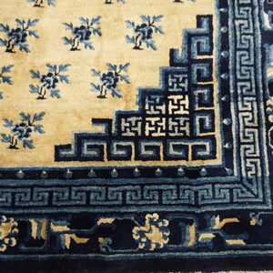 Plush beige rug corner featuring dense blue floral motifs and geometric fretwork borders on light wood flooring.
