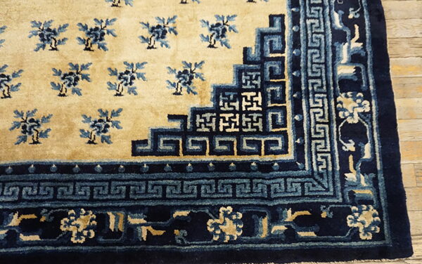 Plush beige rug corner featuring dense blue floral motifs and geometric fretwork borders on light wood flooring.