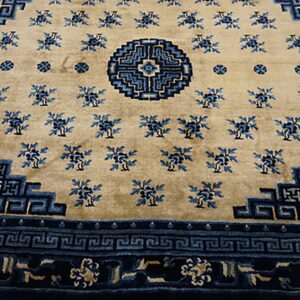 Tan rug with indigo floral motifs, a geometric medallion, and stepped blue borders on wood planks.