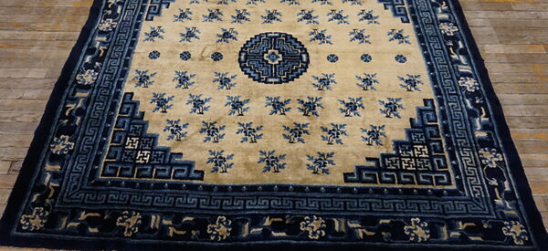 Tan rug with indigo floral motifs, a geometric medallion, and stepped blue borders on wood planks.