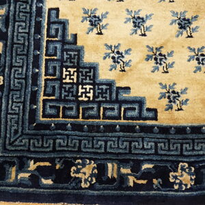 Detail of a tan rug featuring dark blue borders with geometric patterns and lighter blue floral motifs.