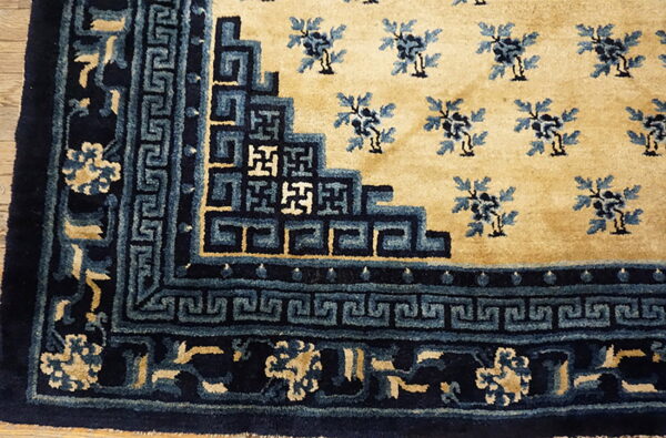 Detail of a tan rug featuring dark blue borders with geometric patterns and lighter blue floral motifs.