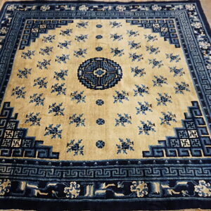Beige field rug with elaborate dark blue borders and scattered floral designs on distressed wood.