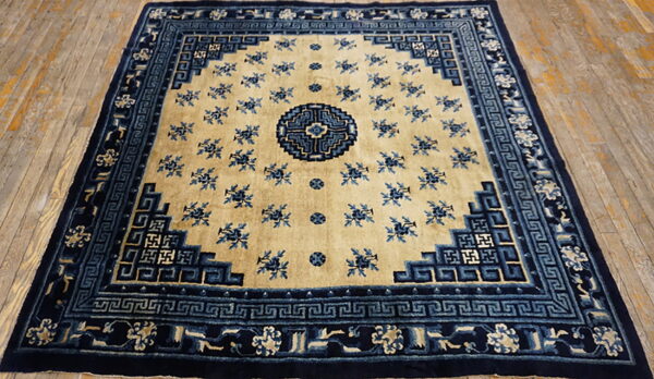 Beige field rug with elaborate dark blue borders and scattered floral designs on distressed wood.