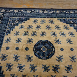Tan rug with navy and light blue geometric borders and scattered floral motifs on wood flooring.