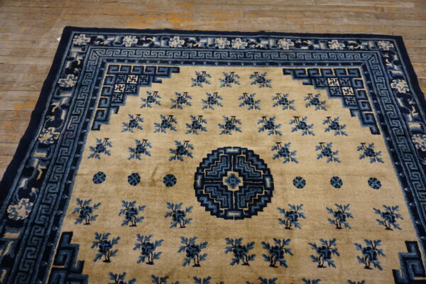 Tan rug with navy and light blue geometric borders and scattered floral motifs on wood flooring.