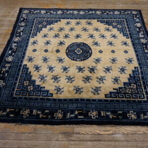 Tan rug with blue floral patterns and intricate navy blue geometric border on rustic wood floors.