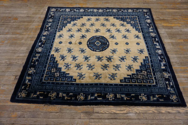 Tan rug with blue floral patterns and intricate navy blue geometric border on rustic wood floors.