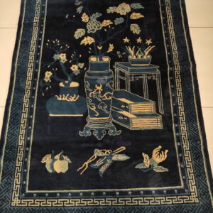 Navy rug with tan and teal pictorial design and geometric meander borders on a white tiled floor.