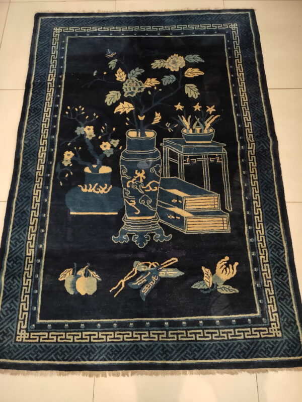 Navy rug with tan and teal pictorial design and geometric meander borders on a white tiled floor.