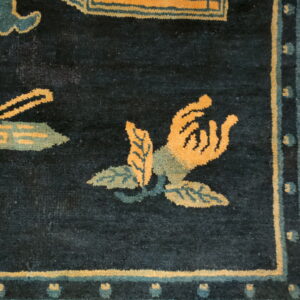Dark blue rug detail showing bright orange and teal floral motifs and a light yellow meander border.