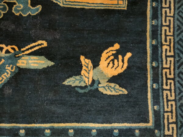 Dark blue rug detail showing bright orange and teal floral motifs and a light yellow meander border.