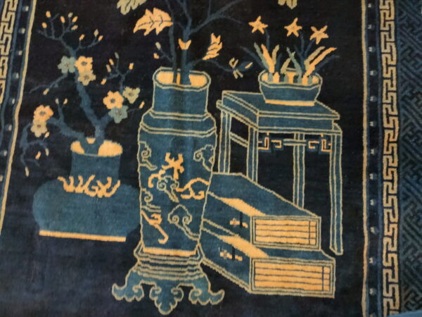 Deep blue high-pile rug displaying an intricate gold and teal pattern of antique vases and stylized flora.