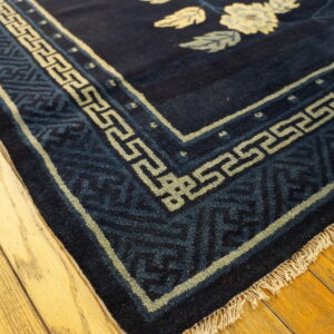 Navy rug corner shows light floral designs and a patterned border on honey-colored wood planks.