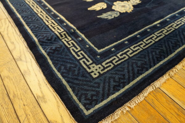 Navy rug corner shows light floral designs and a patterned border on honey-colored wood planks.
