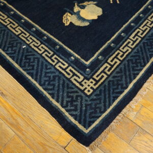 Navy rug corner with pale yellow and blue patterned borders and a fruit motif resting on rustic wood flooring.