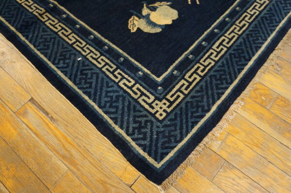 Navy rug corner with pale yellow and blue patterned borders and a fruit motif resting on rustic wood flooring.