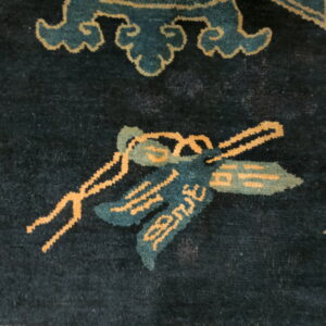 Close-up of a dark indigo rug featuring teal and gold stylized motifs like ribbons and clouds.