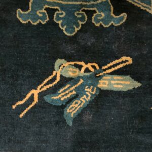 Dark blue rug detail showing bright orange and teal floral motifs and a light yellow meander border.