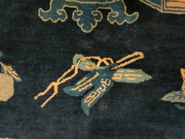 Dark blue rug detail showing bright orange and teal floral motifs and a light yellow meander border.