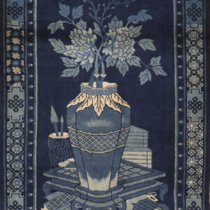 Navy rug with light blue borders and a central floral vase and antiques still life motif.