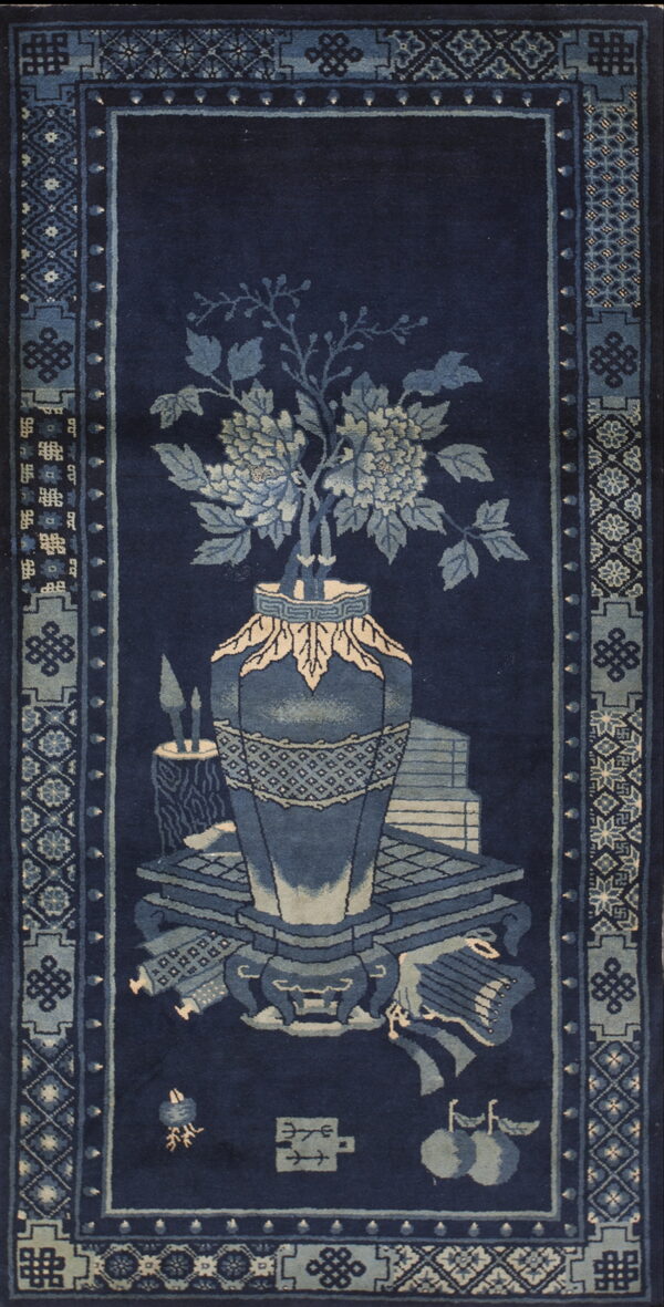 Navy rug with light blue borders and a central floral vase and antiques still life motif.