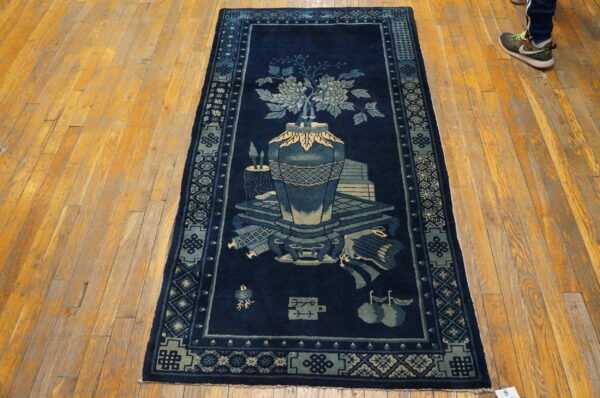 Navy blue rug runner with a pale blue vase and floral motif rests on distressed golden hardwood planks.